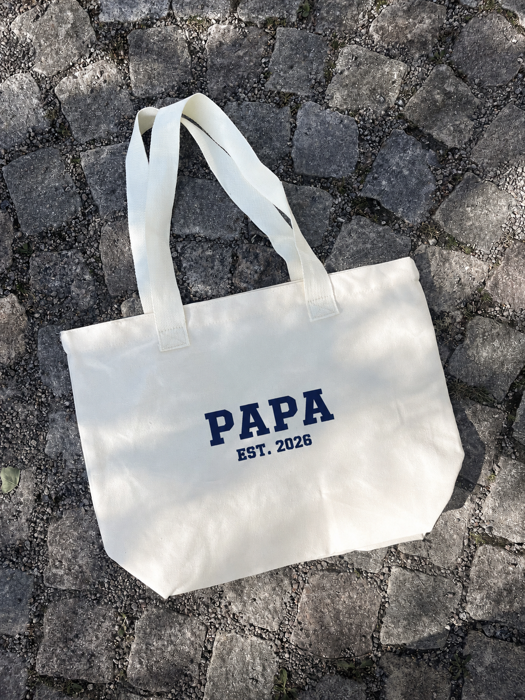 En tygväska med broderad text "Papa Est.2026". 