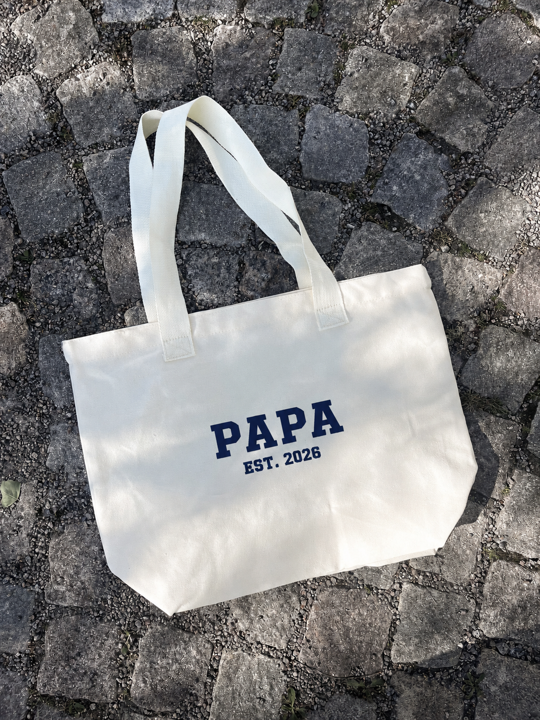 En tygväska med broderad text "Papa Est.2026". 