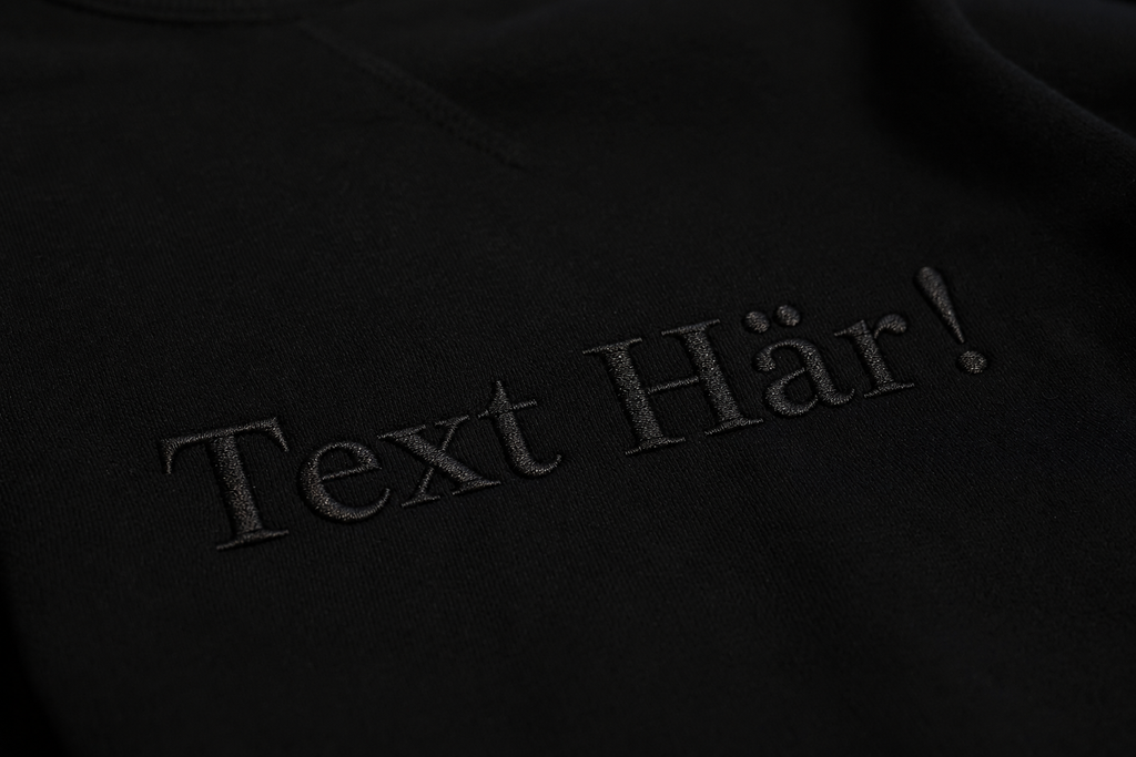 Svart broderad text på svart hoodie. 