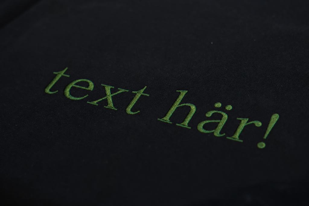 Grön broderad text på t-shirt. 